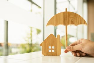 © sommart - stock.adobe.com Foto: Regenschirm und Haus aus Sperrholz